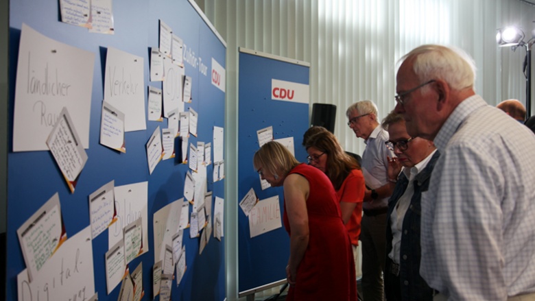 Auf dem Bild sieht man CDU-Mitglieder vor den blauen Pinnwänden, an denen viele Fragen auf Karten hängen.